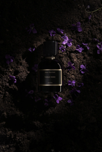 Set on soil and flower petals, Meo Fusciuni Viole Nere Perfume Bottle with cap in dim lighting
