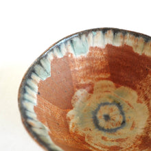 Close-up of a ceramic bowl with brown and blue glaze patterns on a white background