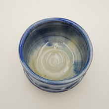 A handmade ceramic bowl with a blue and white glaze, photographed from a top-down perspective on a plain white background.