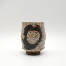 Ceramic cup with speckled glaze and black abstract design on a white background