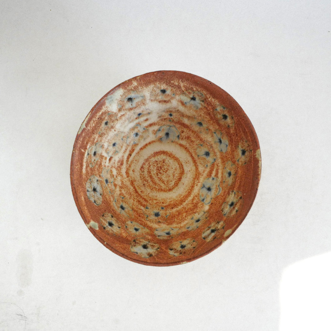 Ceramic bowl with brown and blue floral speckled design on a white background