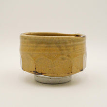 A handmade ceramic bowl with a rustic, organic shape, featuring a textured mustard-yellow and brown glaze, set against a plain light background.