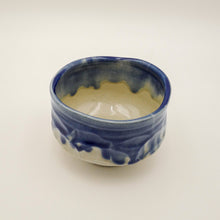 A handmade ceramic bowl with a blue and cream glaze, photographed on a plain off-white background.