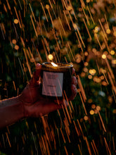Hand holding a lit candle labeled 'Flamingo Estate' against a blurred outdoor background with lights.