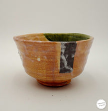 A handmade ceramic bowl with a textured, hand-painted finish. The exterior features a warm ochre-brown glaze with a vertical black patch, while the interior is lined with a dark green glaze.