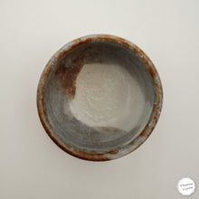 A handmade ceramic bowl viewed from directly above, featuring a rustic brown glazed rim and a matte gray interior with a white center reflection.