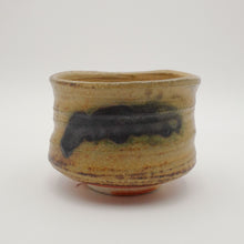 A handmade Japanese ceramic tea bowl with a rustic, hand-painted glaze in warm tan and brown tones, set against a plain light gray background.