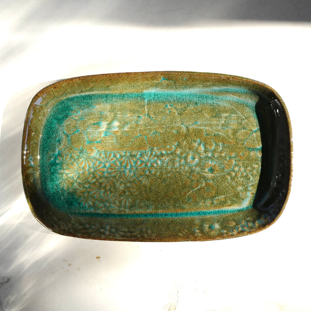 Rectangular ceramic dish with green and brown glaze on a white background
