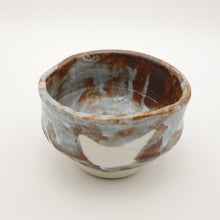 A handmade ceramic tea bowl with a rustic, hand-painted glaze featuring brown, gray, and off-white tones, photographed on a seamless white background.