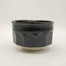 A handmade ceramic tea bowl with a dark charcoal gray textured glaze and a contrasting light beige foot ring, photographed on a neutral light gray background.