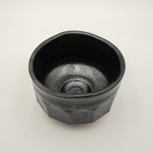 A handmade ceramic tea bowl with a dark charcoal black glaze, photographed on a neutral light gray background.