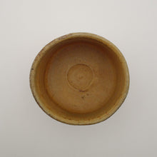 A handmade Japanese ceramic tea bowl with a rustic, hand-painted glaze in warm tan and brown tones, set against a plain light gray background.