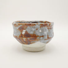 A handmade ceramic tea bowl with a rustic, hand-painted glaze featuring mottled brown, gray, and off-white tones, set against a plain white background.