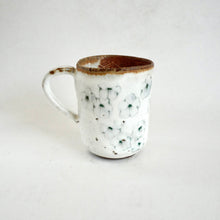 White ceramic mug with brown rim and floral pattern on a white background
