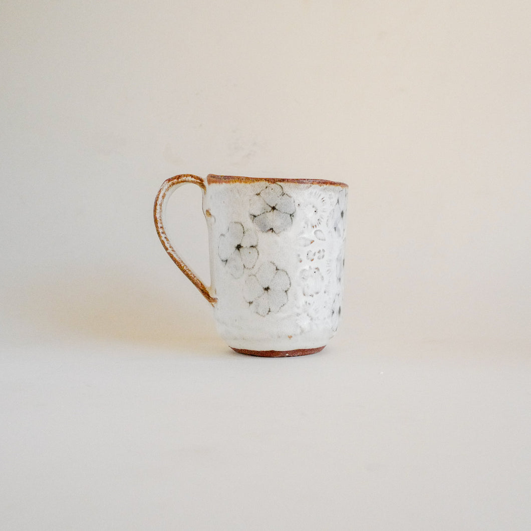 Spako Clay mug, wild flower design with floral texture. Mug handle on left