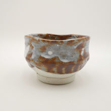 A handmade ceramic tea bowl with a rustic, hand-painted glaze featuring brown, gray, and white tones, set against a plain light background.