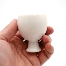 Hand holding a small white ceramic sake cup against a white background