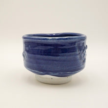 A small ceramic bowl with a glossy cobalt blue glaze and raised decorative figures on the sides, shown on a plain light background.