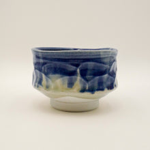 A small ceramic bowl with a textured, wavy glazed surface in deep cobalt blue and white, set against a plain light gray background.