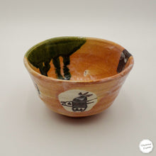 A handmade ceramic bowl with a rustic, hand-painted finish. The exterior glaze is a warm terracotta orange-brown, decorated with a hand-drawn black rabbit illustration on a white circle and a dark brown abstract patch.