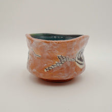A handmade ceramic bowl with a textured terracotta orange exterior, decorated with abstract black, white, and gray geometric patterns, and a dark teal glazed interior, set against a plain light gray background.