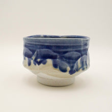 A handmade ceramic tea bowl with a blue and white glaze, featuring a textured, organic wavy pattern, set against a plain light background.