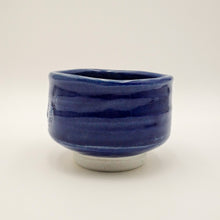 A handmade ceramic tea bowl with a deep cobalt blue glazed finish and a contrasting unglazed light gray base, photographed against a neutral off-white background.