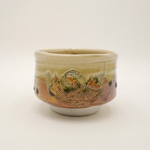 A handmade ceramic matcha bowl with a textured, hand-painted design featuring concentric circles and abstract patterns in earthy tones of brown, orange, and olive green on a cream base.