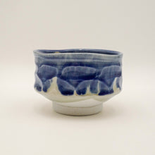 A handmade ceramic tea bowl with a wavy, textured exterior featuring a blue and white glaze, set against a plain light background.