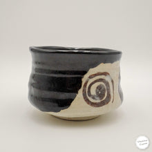 A handmade Japanese-style ceramic tea whisk (chasen) with a glossy black glazed upper half and a textured off-white lower half featuring a brown spiral pattern, set against a plain light gray background.
