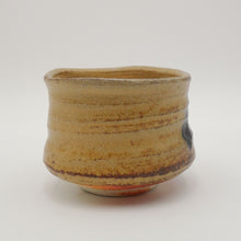A handmade ceramic tea bowl with a rustic, hand-painted glaze in earthy beige, brown, and tan tones, featuring horizontal ridges and a small dark accent on the side, set against a plain light gray background.