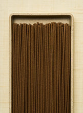 Rectangular container filled with brown incense sticks on a beige background