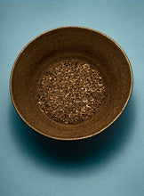 Brown ceramic bowl filled with dark brown potpourri on a blue background