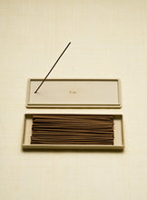 Incense sticks in a porcelain box with one stick out on a beige background