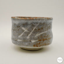 A handmade ceramic matcha tea bowl with a textured gray and brown glaze, featuring white hand-painted brushstrokes on the front, set against a plain light gray background.