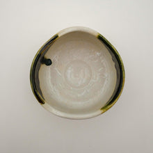 A handmade ceramic bowl viewed from directly above, featuring a glossy off-white glazed interior with subtle hand-painted floral details and dark green glazed accents along the rim.