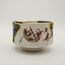 A handmade ceramic tea cup with a textured off-white glaze, featuring hand-painted brown brushstrokes and green glaze accents on the sides, set against a plain light gray background.
