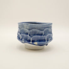 A handmade ceramic tea bowl with a textured, wavy pattern in blue and white glaze, set against a plain off-white background.
