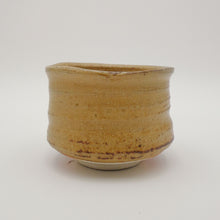 A handmade Japanese ceramic tea bowl with a rustic, hand-painted glaze in warm tan and brown tones, set against a plain light gray background.