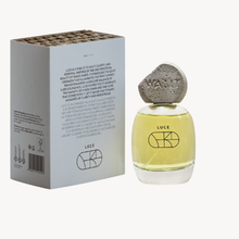 Luce by WA:IT fragrance bottle with pale yellow liquid and a textured stone cap, shown next to its white packaging box on a light gray background.
