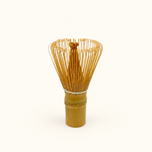 A traditional Japanese bamboo matcha whisk with golden-brown bamboo sections and fine metal tines, centered on a clean white background.