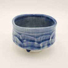 A handmade ceramic tea bowl with a textured, wave-like exterior pattern and a glossy cobalt blue glaze, set against a plain off-white background.