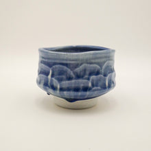A blue and white glazed ceramic tea bowl with a textured, wave-like pattern on the exterior, set against a plain light gray background.