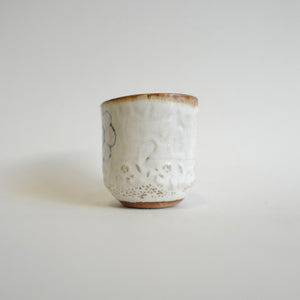 Spako Clay Wide Tumbler single blue flower on white glaze. Foliage texture.