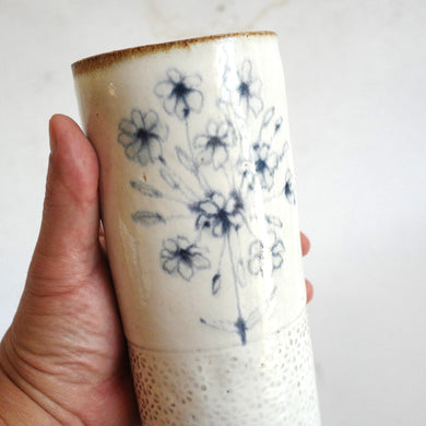 Hand holding a Spako Clay extra Tall Vase blue floral drawing, white glaze