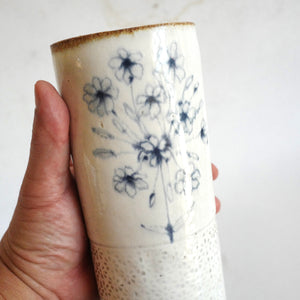 Hand holding a Spako Clay extra Tall Vase blue floral drawing, white glaze