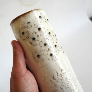 Hand holding Spako Clay extra Tall Vase black floral drawing with floral embossing pattern, white glaze