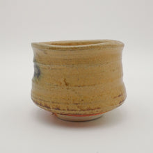 A handmade Japanese ceramic tea bowl with a rustic, hand-painted glaze in warm tan and brown tones, set against a plain light gray background.