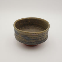 A handmade ceramic tea bowl with a textured, ribbed exterior and a dark, earthy glaze, photographed on a neutral light gray background.