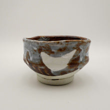 A handmade ceramic tea bowl with a rustic, hand-painted glaze featuring brown, gray, and white colors, set against a plain light gray background.